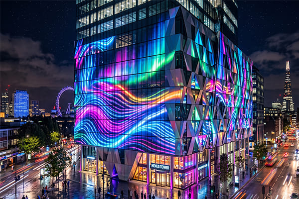 A modern building facade at night with dynamic, colorful interactive lighting that seems to flow across its surface.